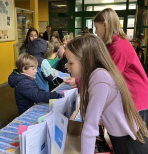 Kinder stehen an einem Verkaufstisch im Flur der Schule. Auf dem Tisch liegen die Exemplare der neuen Ausgabe der Schulzeitung.